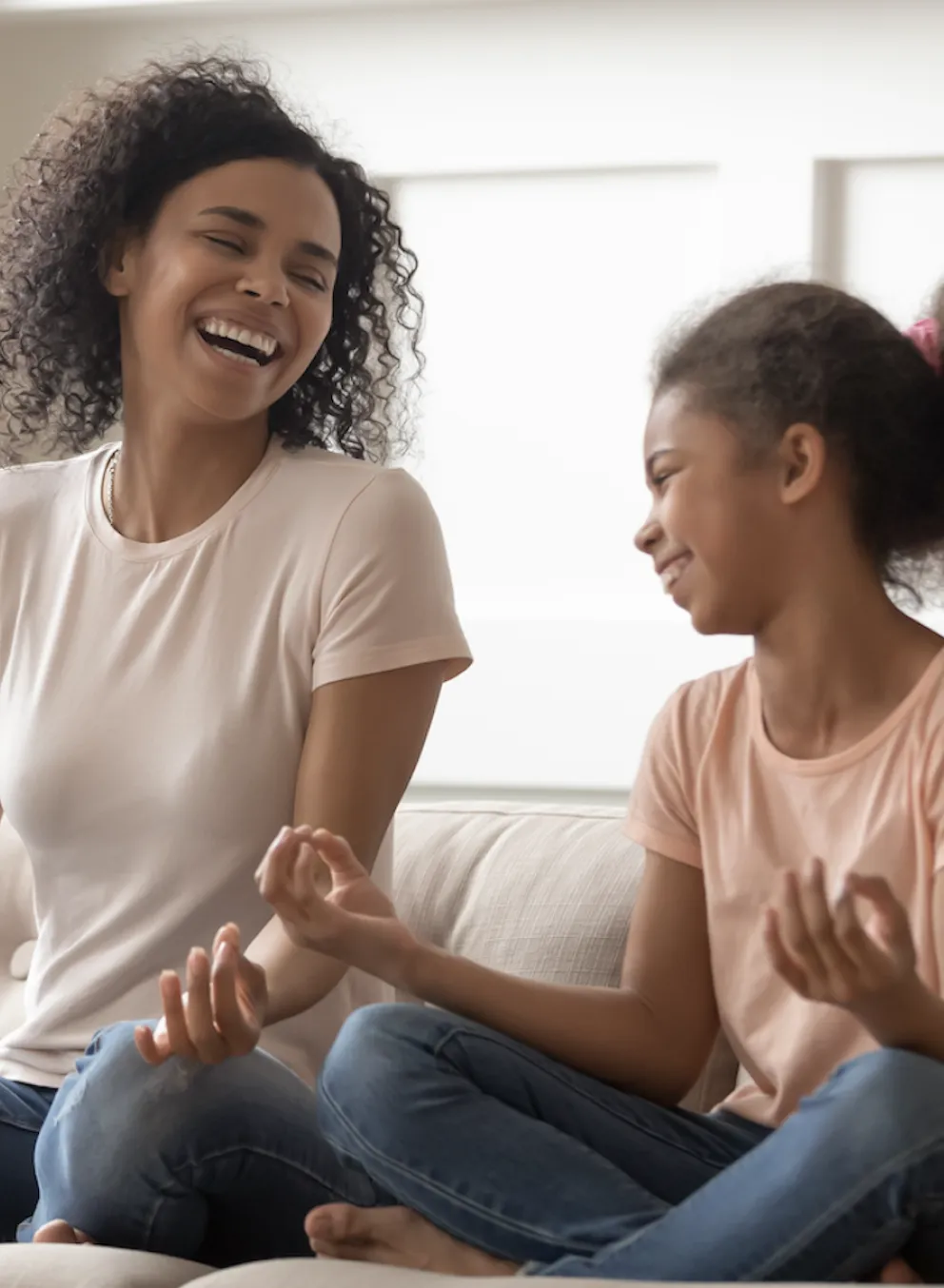 mother and daughter sit on coach laughing with one another