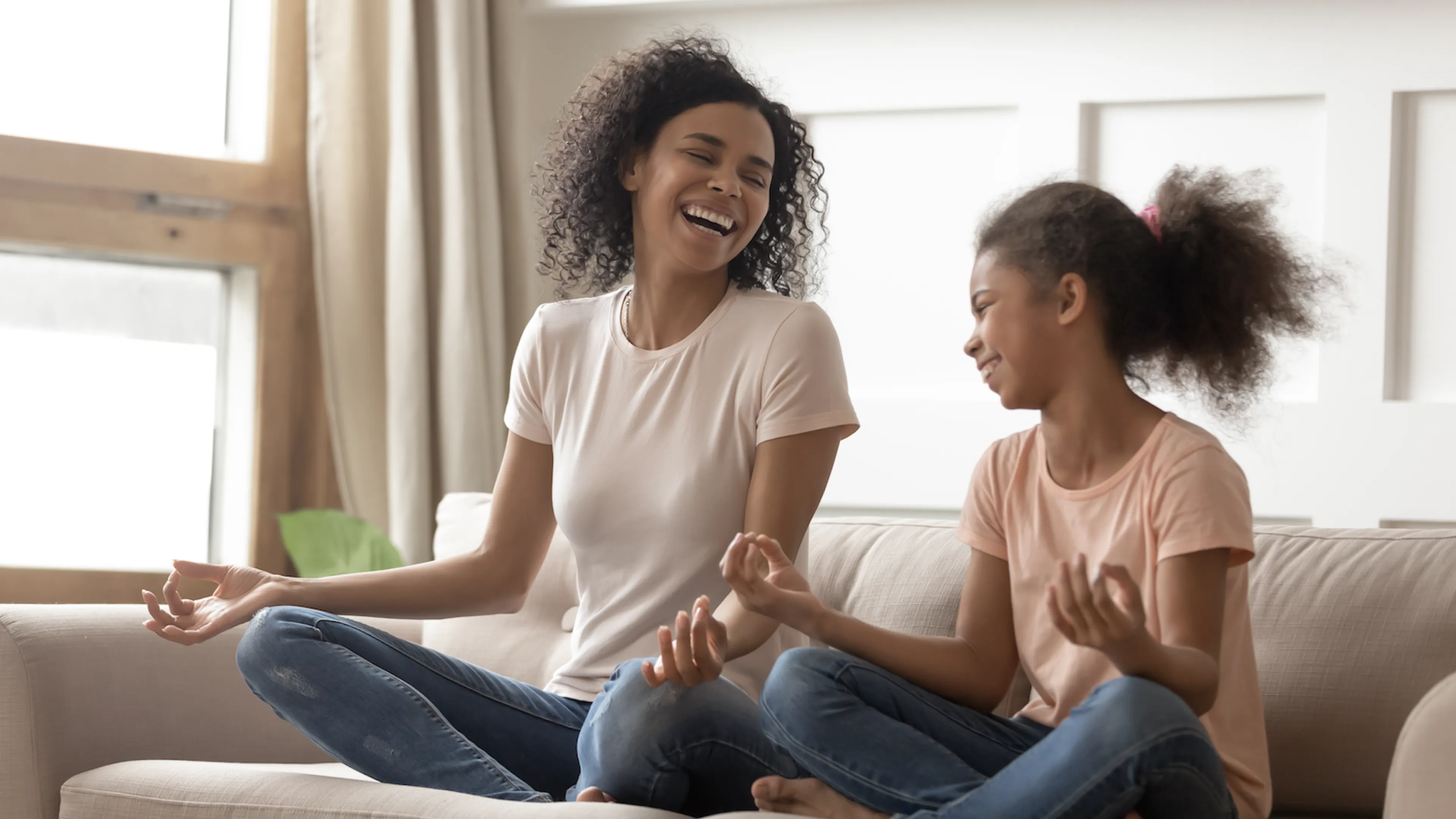 mother and daughter sit on coach laughing with one another