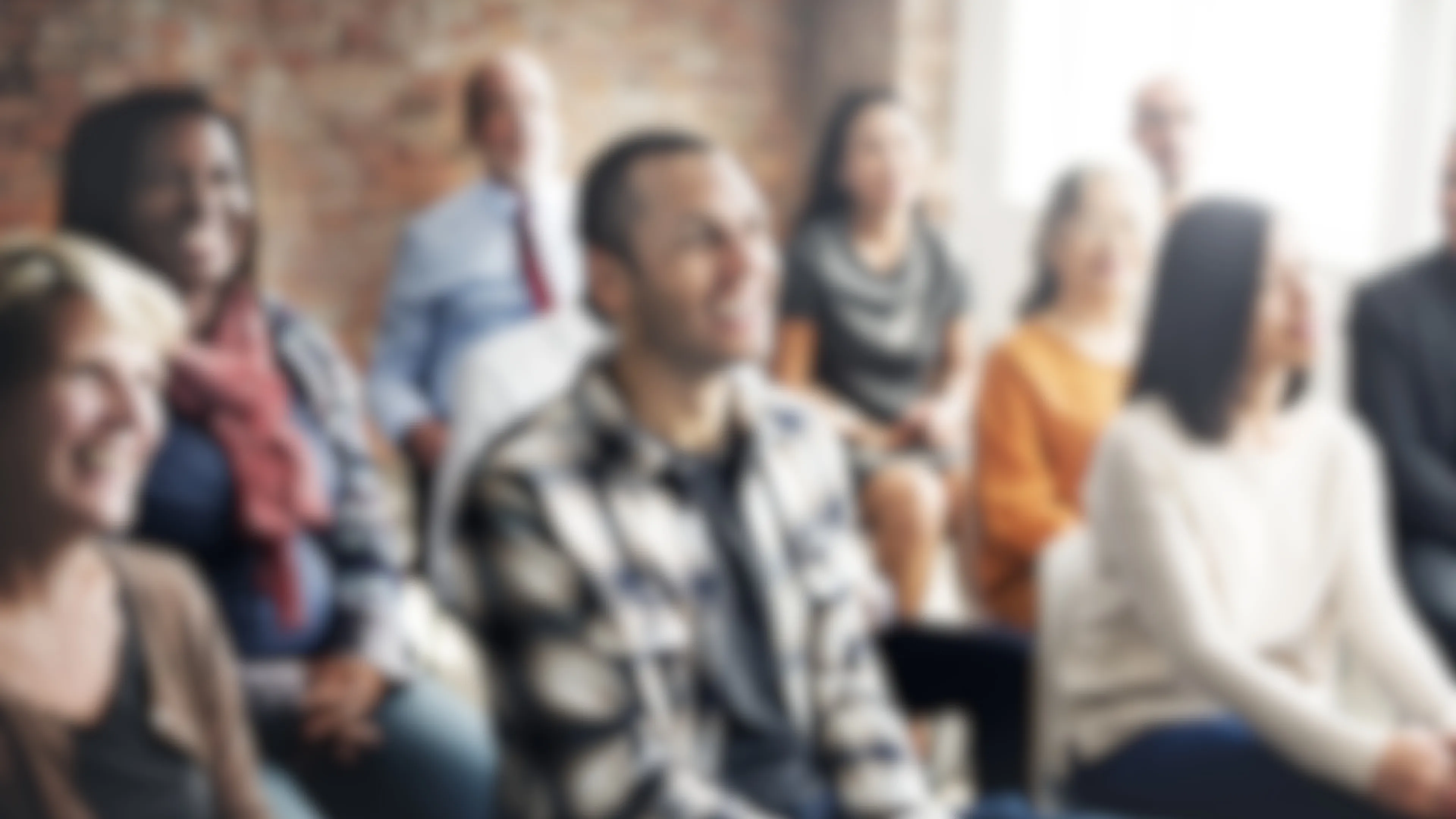Group of diverse adults listening to a speaker and smiling, image is blurred out.
