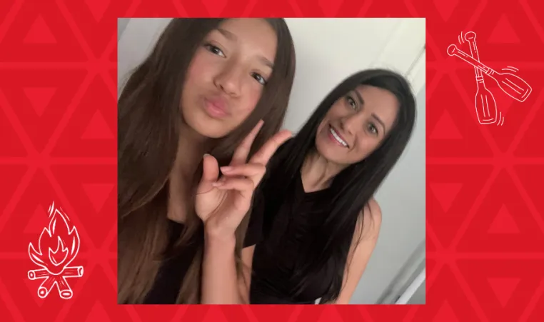 daughter holds up peace symbol with fingers mom smiles in background