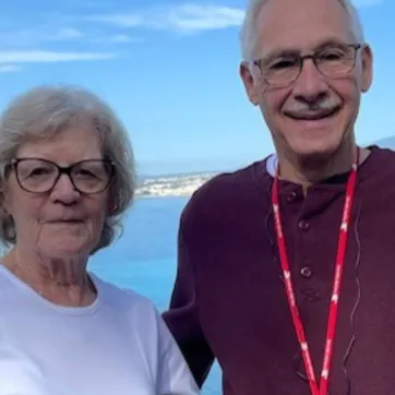 elderly couple stand in front of lake