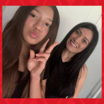 daughter holds up peace symbol with fingers mom smiles in background