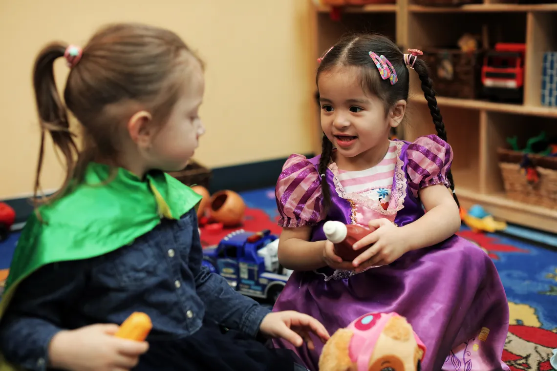 Two female preschool children playing dress up in princess and superhero costumes
